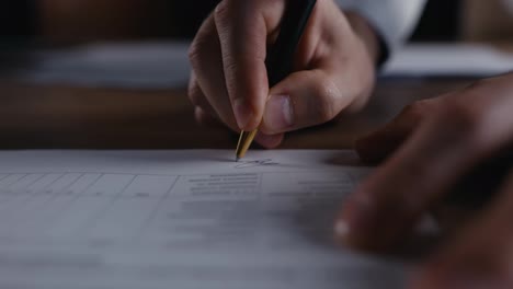 Close-up-of-a-guy-writing-down-a-signature-on-a-piece-of-paper-in-a-document-using-a-black-pen-in-the-office