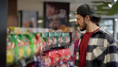 A-confident-brunette-man-in-a-black-cap-examines-goods-on-the-counter-during-his-shopping-in-a-supermarket