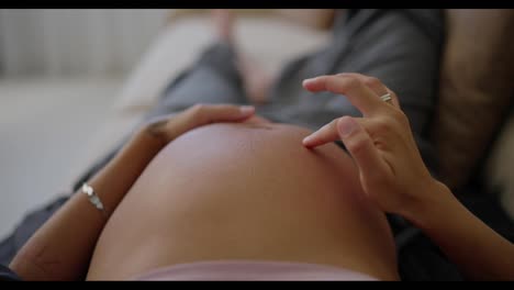 Top-view-close-up-of-happy-pregnant-woman-stroking-her-belly-with-fingers-and-gentle-touches-while-lying-on-sofa-at-home