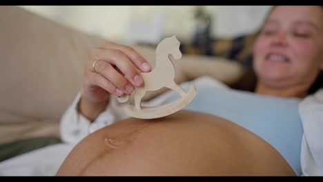 Up-close-a-woman-plays-with-a-small-wooden-toy-on-her-belly-while-pregnant-dreaming-of-her-future-baby