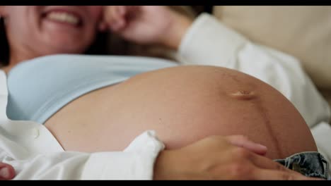 Close-up-of-happy-brunette-pregnant-woman-laughing-big-belly-of-pregnant-woman-stroking-with-hand-at-home