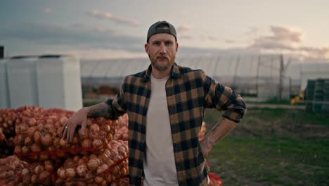 Close-up-portrait-of-a-confident-male-farmer-who-is-leaning-on-bags-of-onions-that-were-collected-during-the-harvest-season-from-the-farm