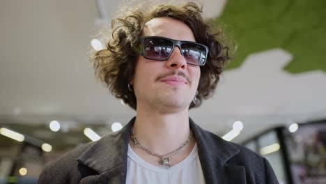 A-confident-and-cool-brunette-guy-with-curly-hair-and-wearing-black-sunglasses-walks-through-the-supermarket-and-looking-around-the-shelves-chooses-the-products-he-needs