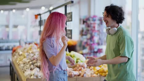 Ein-Glücklicher-Brünetter-Typ-Mit-Weißen-Kopfhörern-Tanzt-Mit-Seiner-Freundin-Mit-Rosa-Haaren-Beim-Allgemeinen-Einkaufen-In-Einem-Supermarkt-In-Der-Nähe-Der-Regale