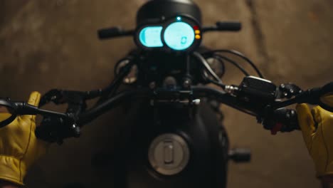 Close-up-top-view-of-a-mechanic-in-yellow-gloves-starting-a-motorcycle-and-inspecting-its-glowing-panel-in-the-workshop