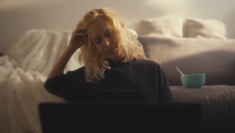 Trauriges-Blondes-Mädchen-In-Einem-Schwarzen-T-Shirt,-Das-Auf-Ihrer-Hand-Zusammengesunken-Ist-Und-Sich-Abends-Zu-Hause-Auf-Dem-Sofa-Einen-Langweiligen-Film-Ansieht