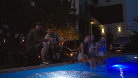 A-group-of-friends-chatting-and-spending-time-near-the-pool-in-a-country-house-during-their-vacation-in-the-evening