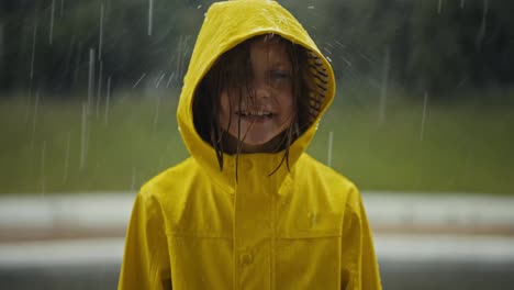 Portrait-of-a-happy-teenage-girl-in-a-yellow-jacket-standing-in-the-rain-and-catching-raindrops-with-her-hood-in-the-park