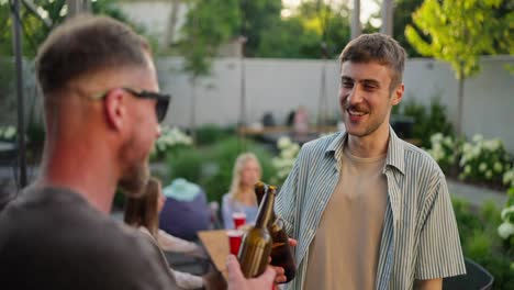 Two-cheerful-guys-chatting-and-having-fun-while-drinking-drinks-from-a-brown-glass-bottle-in-the-courtyard-of-a-house-during-a-weekend-vacation