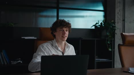 Happy-young-guy-with-curly-hair-in-a-white-shirt-shakes-hands-with-his-interlocutor-during-a-business-conversation-at-a-table-in-the-office