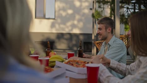 Happy-blond-guy-with-a-mustache-arranges-boxes-of-pizza-and-takes-a-slice-for-himself-during-a-shared-lunch-in-the-courtyard-of-a-country-house