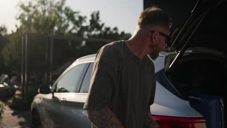 Happy-guy-in-sunglasses-getting-out-of-car-and-taking-things-with-his-girlfriend-before-checking-into-hotel-at-resort-in-summer