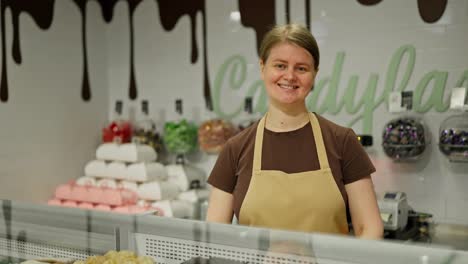 Portrait-of-a-happy-girl-in-a-brown-T-shirt-who-stands-behind-the-counter-in-the-confectionery-department-in-a-supermarket