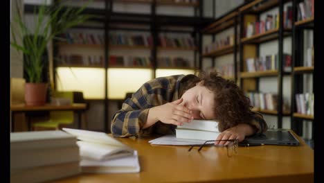 Girl-student-with-curly-hair-sleeps-at-the-table-on-books-in-the-library-after-a-hard-day-at-the-university