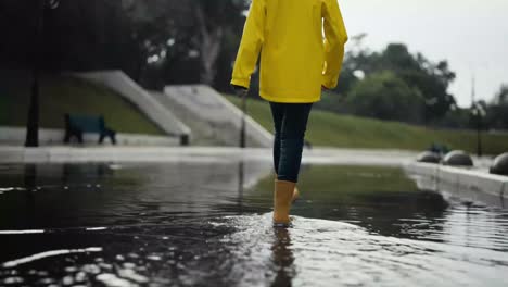 Rear-view-of-a-sad-teenage-girl-in-a-yellow-jacket-and-orange-boots-walking-along-the-street-after-the-rain