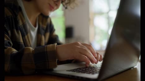 Close-up-of-a-happy-girl-student-in-a-checkered-shirt-typing-on-a-laptop-keyboard-while-sitting-at-a-table-at-the-university