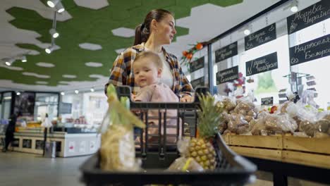 A-happy-brunette-girl-in-a-plaid-shirt-together-with-her-little-daughter-child-walk-around-the-store-and-choose-goods-during-their-shopping-in-the-supermarket