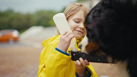 Close-up-a-teenage-girl-in-a-yellow-jacket-gives-a-black-dog-water-from-a-special-drinking-bowl-while-walking-with-her-pet-in-the-park-after-the-rain