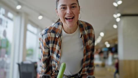 Happy-brunette-woman-in-a-plaid-shirt-leans-on-a-cart-and-spins-during-her-fun-shopping-in-a-supermarket