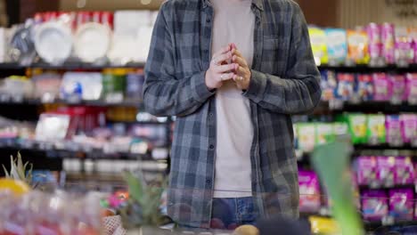 Close-up-of-a-supermarket-visitor-guy-in-a-plaid-shirt-rubbing-his-hands-while-choosing-goods-on-the-shelves-in-the-supermarket