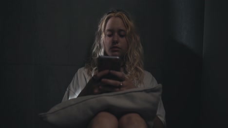 Blondes-Mädchen-Sitzt-Und-Schaut-Sich-Soziale-Netzwerke-Auf-Dem-Telefon-In-Der-Nähe-Einer-Grauen-Wand-An,-Bevor-Es-Zu-Hause-Ins-Bett-Geht