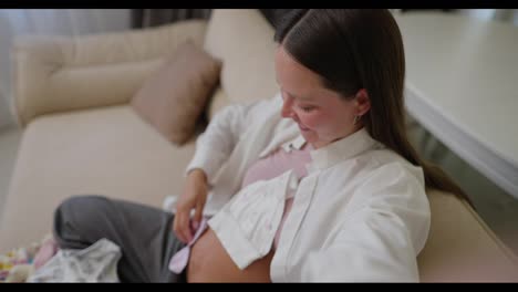 This-first-person-pregnant-brunette-woman-films-a-vlog-and-takes-a-selfie-using-her-phone-showing-clothes-for-her-little-child-whom-she-is-expecting-at-home