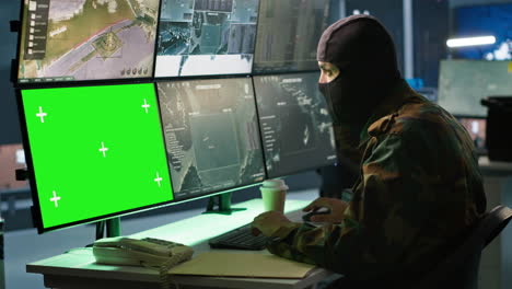 Special-forces-spy-examining-data-in-monitoring-room-with-chroma-key-monitors