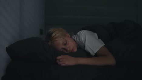 A-young-blonde-girl-in-a-white-T-shirt-wakes-up-abruptly-while-lying-in-a-serious-bed