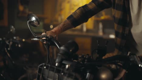 Close-up-a-bike-guy-in-a-checkered-shirt-takes-out-a-repaired-motorcycle-from-his-studio-workshop