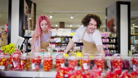 Zwei-Supermarktmitarbeiter,-Ein-Brünetter-Mann-Und-Ein-Mädchen-Mit-Rosa-Haaren,-Machen-Eine-Bestandsaufnahme-Der-Waren-In-Der-Obstabteilung