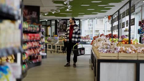 Side-view-of-a-thoughtful-man-in-a-black-cap-examining-the-supermarket-shelves-and-choosing-the-goods-he-needs-during-his-shopping