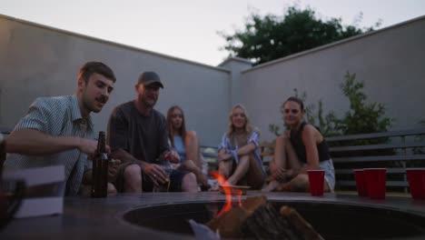 A-confident-blond-guy-lights-a-fire-in-a-barbecue-while-relaxing-and-partying-in-the-courtyard-of-a-country-house-during-twilight