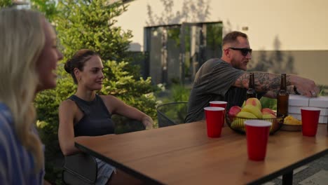 Confident-Guy-in-sunglasses-and-a-gray-T-shirt-opens-boxes-of-pizza-during-a-shared-lunch-at-a-table-in-the-courtyard-of-a-country-house