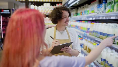 Over-the-shoulder-a-girl-with-pink-hair-points-to-a-guy-supermarket-worker-while-taking-inventory-together-in-a-supermarket