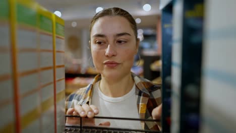 Close-up-a-confident-brunette-girl-in-a-checkered-shirt-examines-the-goods-on-the-counter-and-chooses-the-product-she-needs-in-the-supermarket