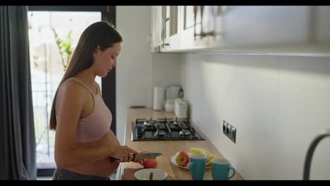 Mujer-Morena-Embarazada-Colgando-Fruta-Para-Ensalada-De-Frutas-Por-La-Mañana-En-La-Cocina-Antes-Del-Desayuno