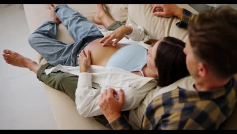 Top-view-of-a-happy-pregnant-brunette-woman-lying-on-her-husband-legs-and-relaxing-while-lying-on-the-sofa-in-a-modern-apartment