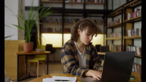 Glückliches-Mädchen-Mit-Lockigem-Haar-Macht-Ein-Aufwärmtraining,-Während-Sie-In-Einer-Universitätsbibliothek-An-Einem-Laptop-Arbeitet