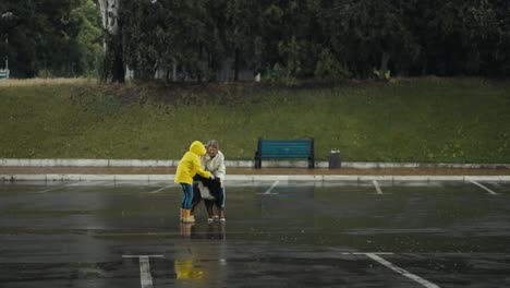 Happy-blonde-woman-in-a-white-jacket-together-with-her-daughter-in-a-yellow-jacket-playing-with-their-big-black-dog-during-the-rain-in-the-park