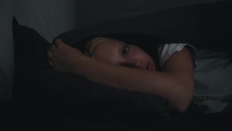 Portrait-of-a-blonde-girl-in-a-white-T-shirt-who-sharply-falls-her-head-in-bed-and-covers-herself-with-a-blanket-at-night