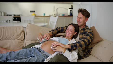 Joyful-man-and-woman-putting-wireless-headphones-on-pregnant-woman-tummy-while-relaxing-at-home