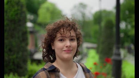 Portrait-of-a-happy-brunette-girl-with-curly-hair-who-puts-on-wireless-white-headphones-and-poses-in-the-park