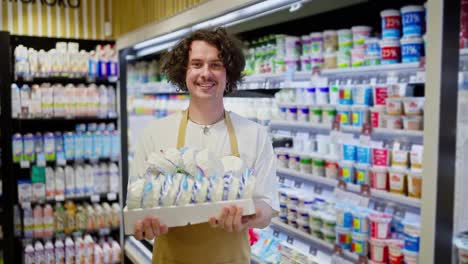 Portrait-of-a-happy-guy-holding-in-his-hands-a-box-of-cottage-cheese-and-other-dairy-products-in-a-department-in-a-supermarket