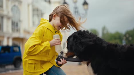 Happy-teenage-girl-feeds-her-dog-from-a-special-drinking-bowl-during-a-walk-after-the-rain