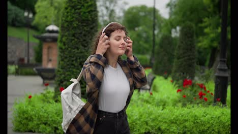 Chica-Morena-Feliz-Con-Auriculares-Posando-Mientras-Camina-Por-El-Parque.-Terminando-Las-Clases-En-La-Universidad-Y-Dando-Un-Paseo-Al-Aire-Libre.