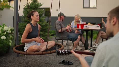 über-Die-Schulter-Klatscht-Ein-Glückliches-Brünettes-Mädchen-Und-Singt-Lieder-Zu-Der-Melodie,-Die-Ihr-Freund-Auf-Der-Gitarre-Spielt,-Während-Einer-Party-Mit-Seiner-Firma-Im-Hinterhof-Eines-Landhauses