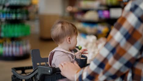 Close-up-of-a-little-girl-baby-sitting-in-a-cart-during-a-trip-to-the-supermarket-and-shopping-with-her-mom