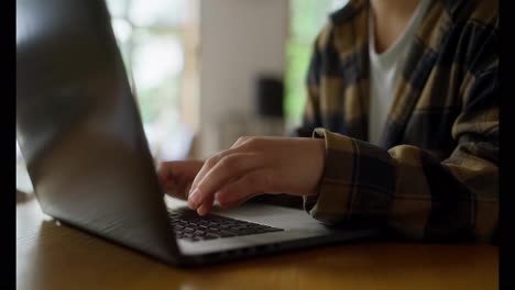 Close-up-of-a-girl-in-a-plaid-shirt-typing-on-a-laptop-keyboard-while-sitting-at-a-table-in-the-library