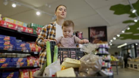 Ein-Kleines-Mädchen-Sitzt-In-Einem-Einkaufswagen-Und-Schaut-Sich-Alles-An,-Während-Sie-Mit-Ihrer-Mutter-Im-Supermarkt-Einkauft