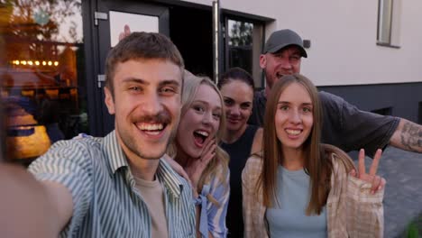 A-cheerful-blond-guy-takes-a-selfie-with-his-friends-having-fun-and-posing-in-the-courtyard-of-a-country-house-during-his-vacation